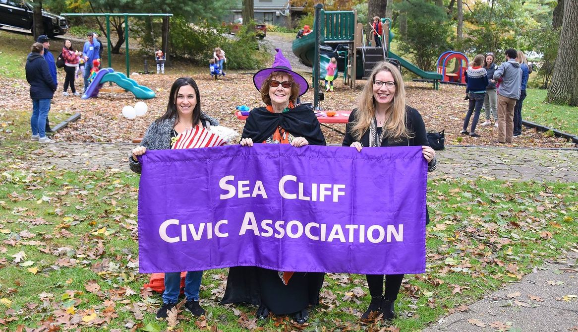 Volunteers holding the purple Sea Cliff Civic Association banner in Central Park, one dressed as a witch
